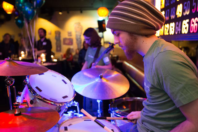 Drummer in a beanie playing at the Love Bomb 2017 event, with colorful lighting and balloons in a lively atmosphere, supporting My Voice Music nonprofit.